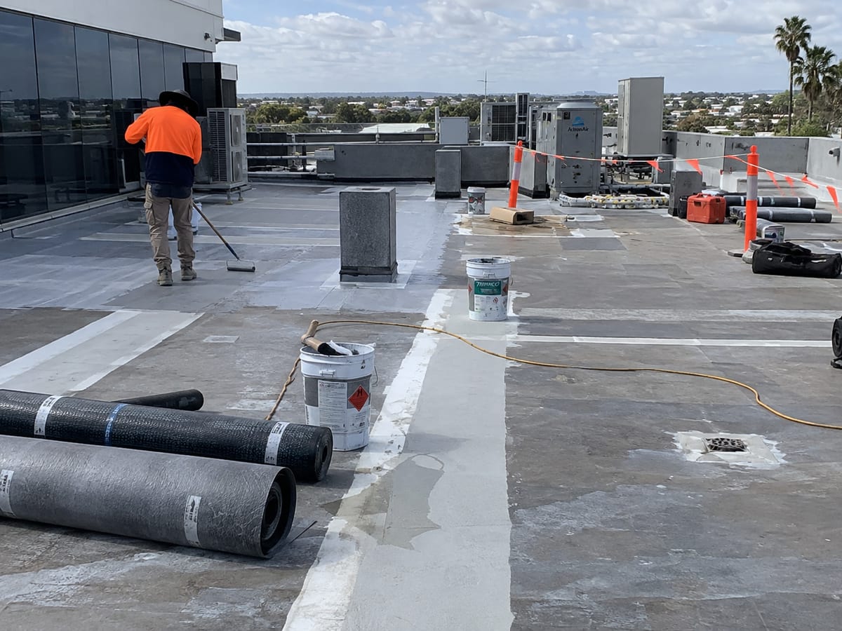 Worker applying waterproofing on a commercial roof around rooftop equipment